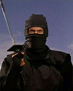 a man wearing a black mask and holding a stick in his hand with the sky behind him