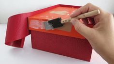 a person is holding a paintbrush and painting the inside of a red gift box