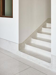 a white staircase leading up to a window in a room with concrete floors and walls