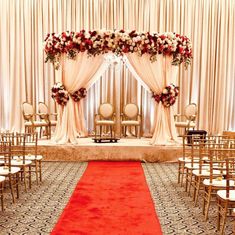 a wedding ceremony setup with red carpet and white drapes, gold chairs and flowers