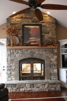 a living room with a stone fireplace and ceiling fan