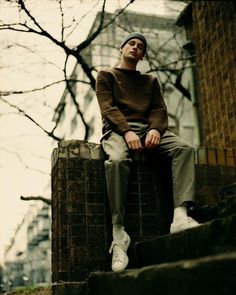 a young man sitting on top of a brick wall next to a tree and building