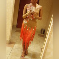 a woman standing in front of a mirror looking at her cell phone and wearing an orange fringe skirt