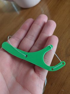 a green pair of scissors being held in someone's hand on a wooden table