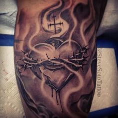 a tattoo on the arm of a man with a cross and heart in flames behind it