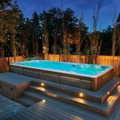 an outdoor hot tub lit up at night with lights on the deck and steps leading to it