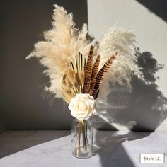 a vase filled with flowers and feathers on top of a white countertop next to a wall