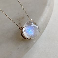 "ITEM DESCRIPTION: >>The pendant is made from Solid 14K Yellow Gold. Gemstone used is absolutely natural and ethically sourced.  >>Natural Rainbow Moonstone in Cabochon round shape with a beautiful blue sheen in prong setting is studded on it with utmost precision.  >>This is a minimalist design and is absolutely hassle-free and everyday jewelry.  Gem: Rainbow Moonstone Gem size: 15x15mm round  Gem weight: 11.80 carats Gold purity: 14K (58.33% approx.) Gold weight: 1.48 grams  Gross weight: 3.84 grams The pendent comes with 16 \" inches adjustable chain. The Gold purity is guaranteed and it comes with authentic 14K gold hallmark. Since these Pendants are handmade, they are Nickel/Lead FREE.  CUSTOMISATION: --> The same pendant can be made with a thicker bezel as well. --> You can choose yo Celestial Moonstone Gemstone Necklace, Moonstone Gemstone Round Pendant Jewelry, Celestial Moonstone Round Pendant Jewelry, Moonstone Gemstone Jewelry With Round Pendant, Moonstone Round Necklace For Anniversary, Unique Moonstone Round Necklace, Unique Round Moonstone Necklace, Formal Moonstone Round Necklace, Formal Round Moonstone Necklace