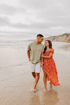 an engaged couple standing on the beach in front of the ocean during their engagement session