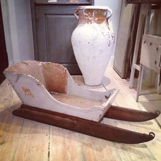 an old wooden sleigh sitting on the floor next to a large white vase