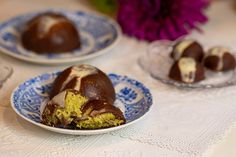 two plates with chocolate covered desserts on top of a white tablecloth and purple flowers in the background