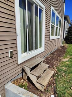 a wooden bench sitting in front of a window next to a grass covered yard and house