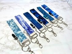 six blue and white lanyards with metal chains on marble counter top, one has a key chain attached to it