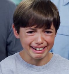 a young boy smiling and wearing a gray shirt