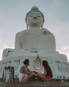 two people sitting in front of a large statue