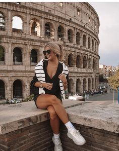 a woman sitting on top of a brick wall next to an old roman collise