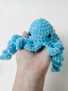 a hand holding an octopus stuffed animal in it's right hand, with its eyes open