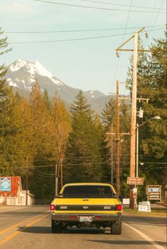 a yellow truck is driving down the road in front of some mountains and telephone poles