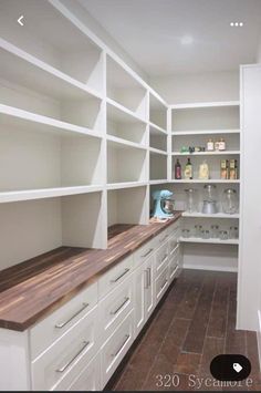 an empty pantry with white cabinets and wood counter tops, along with lots of shelves