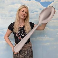 a woman standing in front of a painting holding a large spoon over her shoulder and looking at the camera