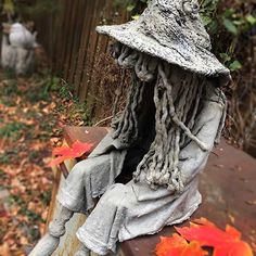 a scarecrow sitting on top of a wooden bench next to leaves and a fence