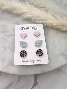 three pairs of leopard print and heart shaped studs on top of a white marble surface