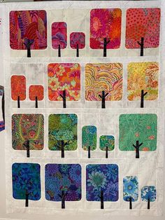 a quilted wall hanging with many different designs on it's sides and trees in the middle