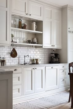 a kitchen with white cabinets and wooden chairs in the corner, along with an area rug on the floor