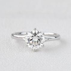 a white gold engagement ring with a round brilliant cut diamond in the center, on a plain surface