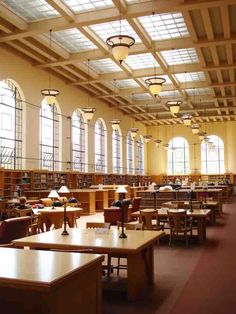 an empty library filled with lots of tables and chairs next to tall windows in the ceiling