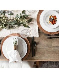 the table is set with white plates and silverware, napkins and greenery