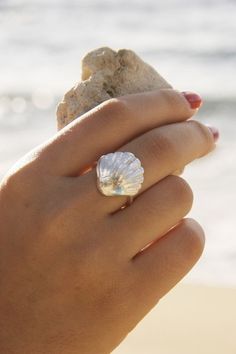 a woman's hand holding a shell on the beach