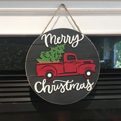 a merry christmas sign hanging from the side of a window with a red truck carrying a tree