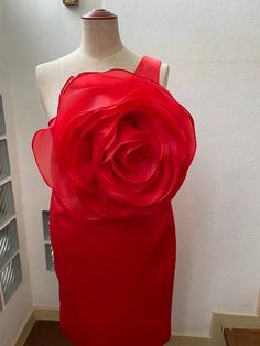 a mannequin wearing a red dress with a large rose on the top and bottom