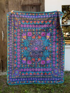 a purple and blue quilt hanging on a wooden fence next to a white building with a brown door