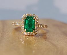 an emerald and diamond ring sitting on top of a wooden table