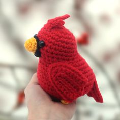 a crocheted red bird sitting on top of a finger