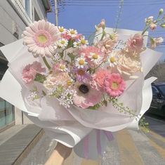 a bouquet of pink and white flowers is held by someone's hand on the street