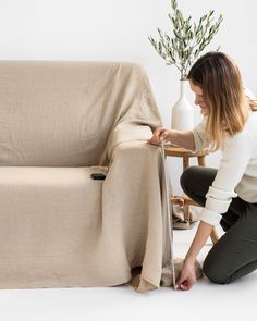 a woman is measuring the length of a couch with a tape and a vase behind her