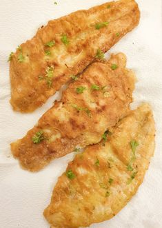 three pieces of fried fish sitting on top of a white paper towel with green garnishes