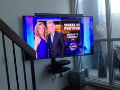 a television screen with a news anchor on it in front of a stair case next to a window