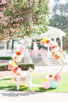 a white horse and some balloons in the grass near a gazebo with pink flowers on it