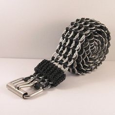 a black and silver chain belt with metal buckles on white table top next to wall