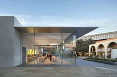 people are walking through an open area with glass walls on either side of the building