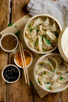 three bowls filled with dumplings next to dipping sauces and chopsticks on a wooden table