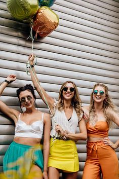 three women standing next to each other holding balloons