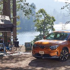 an orange car parked in front of a tent next to a body of water and trees