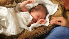 a woman holding a baby wrapped in a blanket while laying on top of some hay