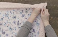 two hands are holding the edge of a baby's crocheted blanket on a wooden floor