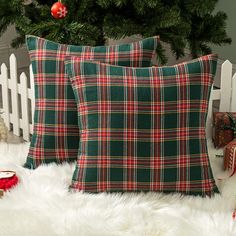 two green and red plaid pillows sitting on top of a white fur covered floor next to a christmas tree